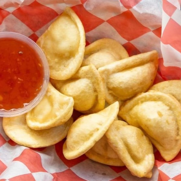 Golden fried dumplings in a red and white checkered basket with a side of sweet chili sauce.