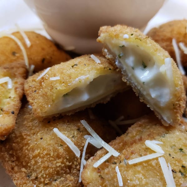 Close-up of golden-brown fried ravioli, one split open revealing creamy white filling, topped with grated cheese.