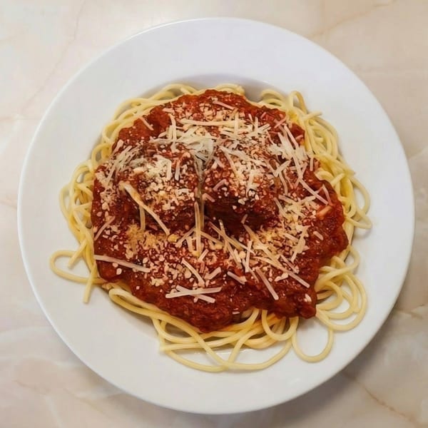 Spaghetti with meatballs and marinara sauce, topped with grated Parmesan cheese on a white plate.