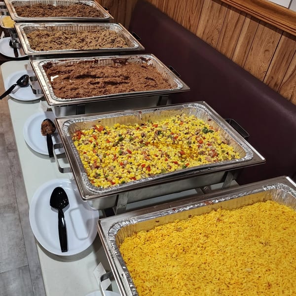 A buffet line with several chafing dishes filled with various hot foods, including rice, corn, and meats.